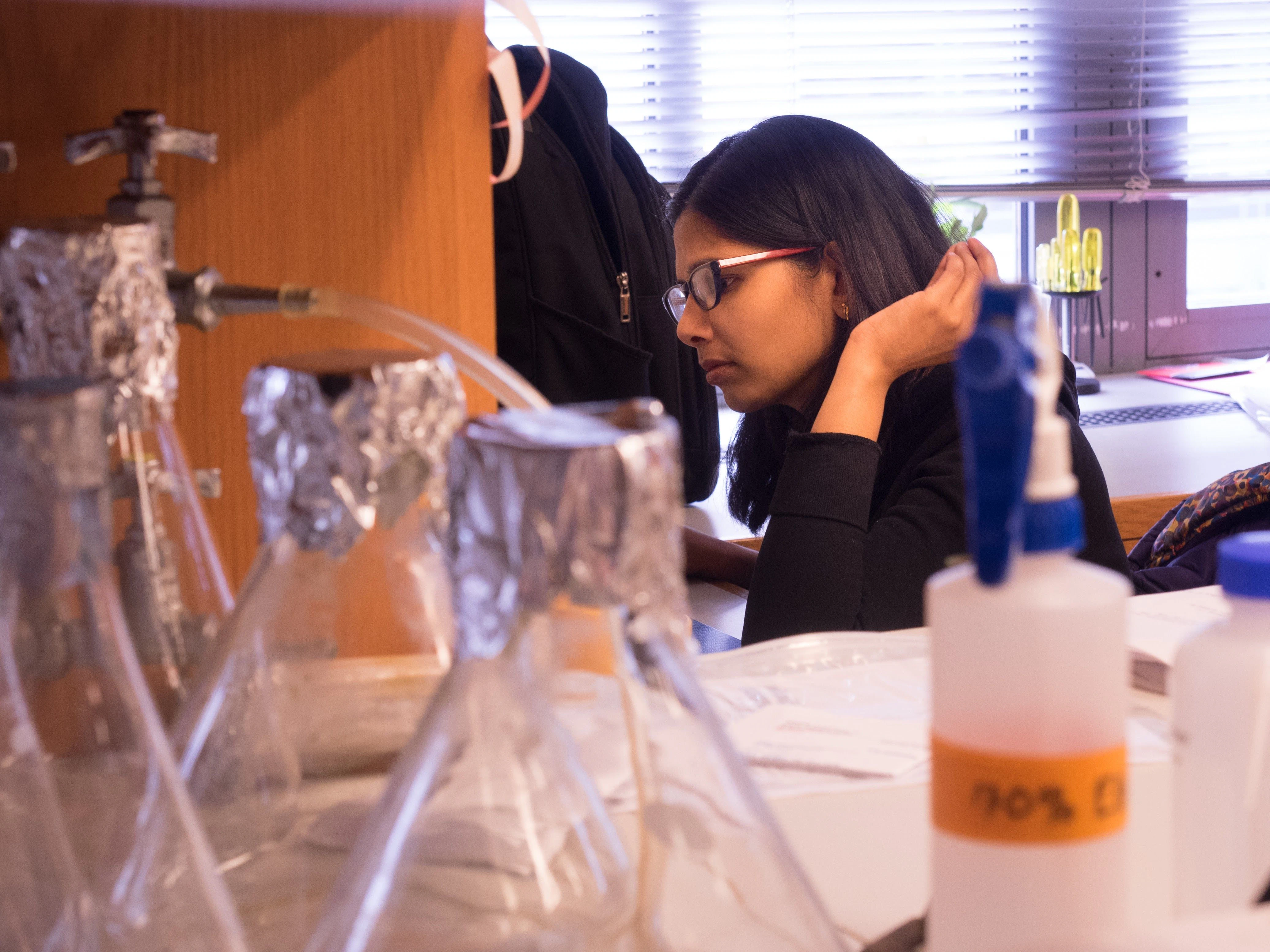 female student with glasses, pictured in a lab setting with beakers