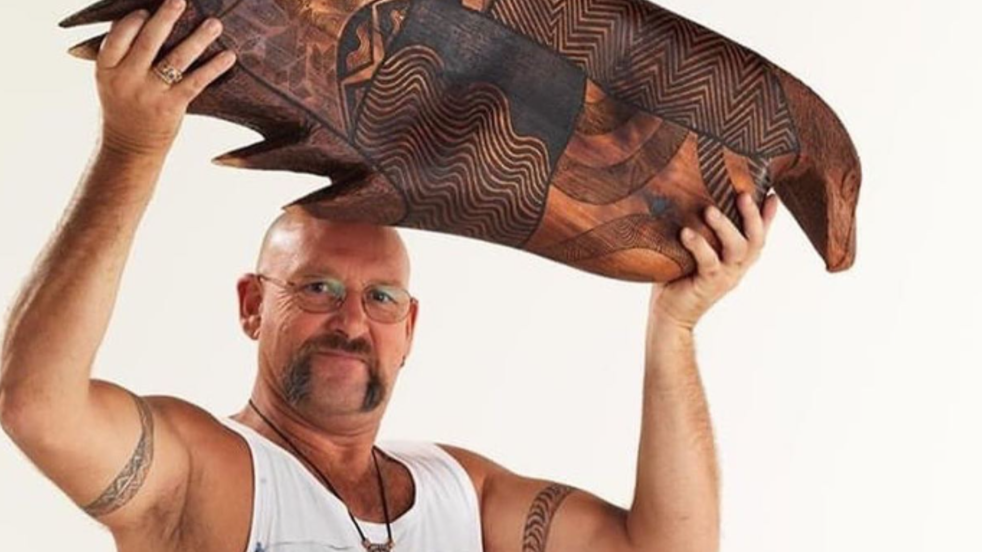 Mick Harding artist holding Indigenous wood carving above his head